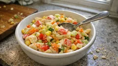 Sałatka warzywna z kukurydzą, papryką i ogórkiem w białej misce na blacie kuchennym.