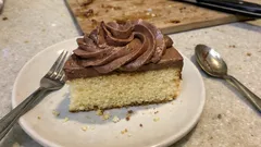 Kawałek ciasta z czekoladowym kremem na talerzu, widelczyk i łyżeczka obok.