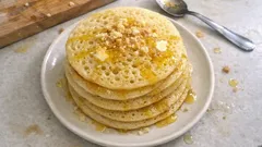 Stos marokańskich naleśników baghrir z miodem i orzechami na białym talerzu.