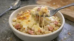 Zapiekanka z serem, szynką i ziemniakami w misce, rozciągający się ser na widelcu