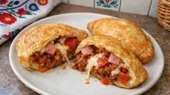 Pieczone pierogi z nadzieniem mięsnym i serem na białym talerzu, kuchnia polska.