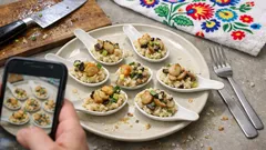 Przystawki na łyżkach, osoba robi zdjęcie jedzenia telefonem, kolorowy obrus w tle.