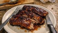 Pieczone żeberka wieprzowe na białym talerzu, obok widelec i nóż, domowy posiłek.