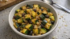 Sałatka z cukinii, bakłażana i oliwek w białej misce na szarym blacie kuchennym.