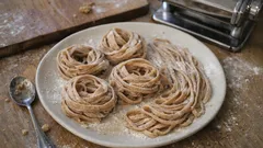 Domowy makaron tagliatelle na białym talerzu, mąka i maszynka do makaronu na stole