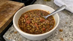 Zupa z soczewicy w białej misce na kuchennym blacie, z łyżką w środku.