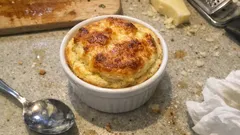 Francuskie suflet serowy w białej kokilce na kuchennym blacie, obok łyżka i ser.