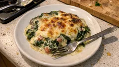 Zapiekanka ze szpinakiem, szynką i serem na białym talerzu, domowe danie