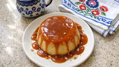 Deser budyniowy z polewą karmelową na talerzu, obok filiżanka i ludowa serwetka.