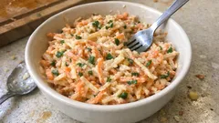 Sałatka z marchewką i selerem w misce na stole, widoczny widelec i łyżka obok.