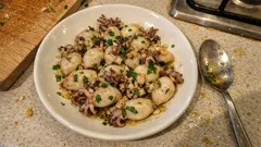 Gotowane ośmiorniczki na talerzu, posypane ziołami, na kuchennym blacie.