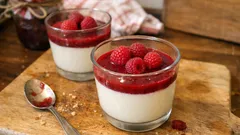 Deser panna cotta z musem malinowym podany w szklankach na drewnianej desce