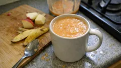 Kubek z koktajlem owocowym na blacie kuchennym, obok pokrojone jabłka i banan.