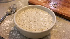 Zakwas na chleb w misce, przygotowanie ciasta na domowy chleb, mąka na stole.