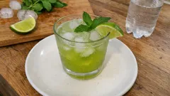 Mojito z limonką, miętą i lodem na talerzu, orzeźwiający drink na drewnianym stole