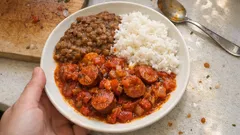 Danie z białym ryżem, kiełbasą w sosie pomidorowym i gotowaną fasolą na talerzu.