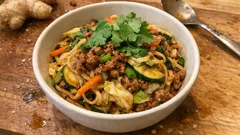 Makaron z mięsem mielonym, warzywami i kolendrą w białej misce na desce do krojenia