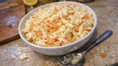 Sałatka coleslaw w białej misce na blacie kuchennym, obok łyżka i plaster cytryny
