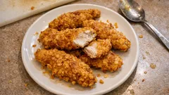 Chrupiące stripsy z kurczaka w panierce na białym talerzu, domowy fast food