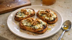 Grzanki z serem pleśniowym i orzechami włoskimi na białym talerzu na stole.