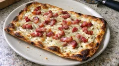 Tarte flambée z boczkiem i cebulą na białym talerzu, danie kuchni alzackiej